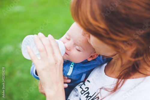 Young mom feeding her sleepy smiling son toddler with bottle