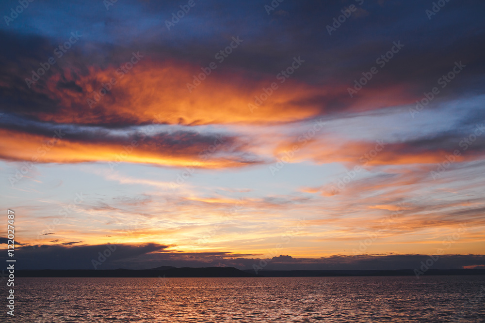 Bright coloured sunset behind clouds and island in ocean