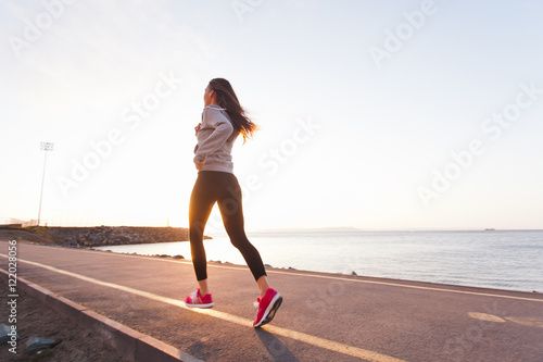 Young woman athlete runs at sunset on seashore sidewalk