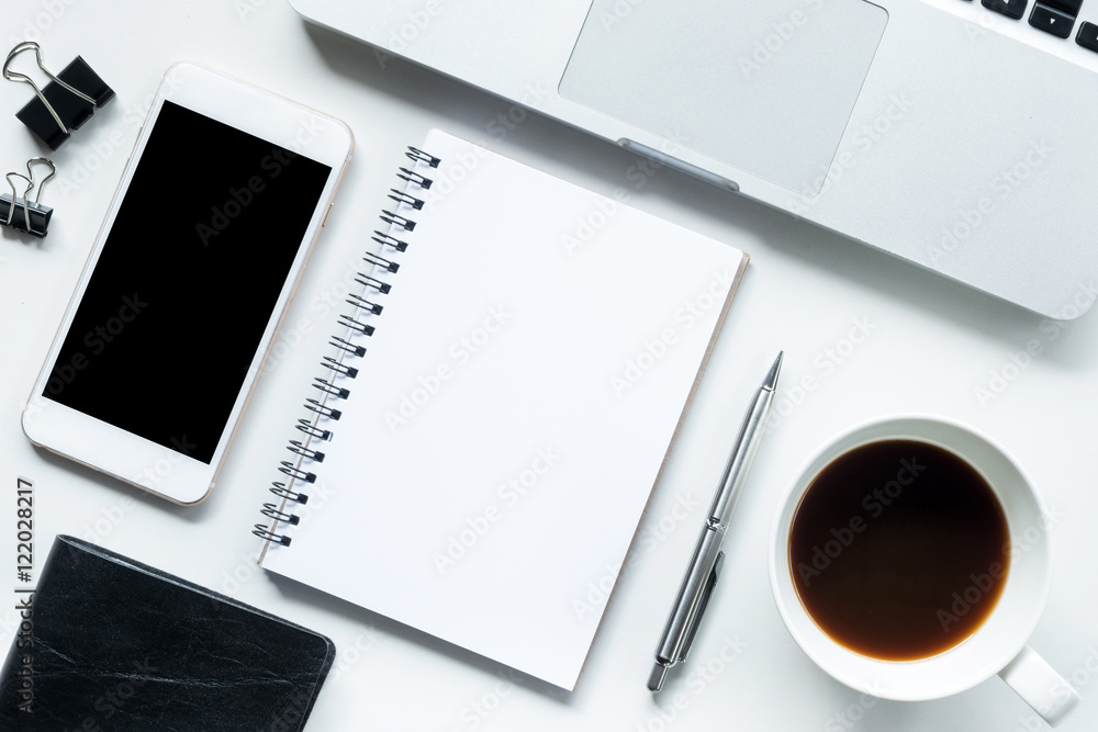 White office desk table with notebook, laptop, coffee and suppli White office desk table with notebook, laptop, coffee and suppli