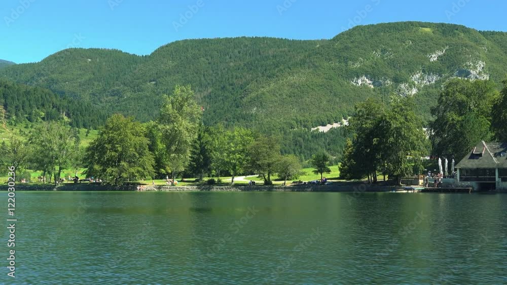 View on the Bohinj lake surrounding area from sailing tourist boat on bright sunny summer day View on the Bohinj lake surrounding area from sailing tourist boat on bright sunny summer day