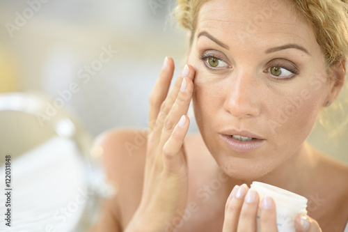 Middle-aged blond woman putting cosmetics on