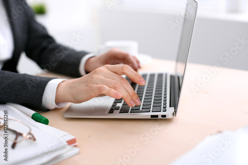 Close up of business woman hands typing on laptop computer in the white colored office.