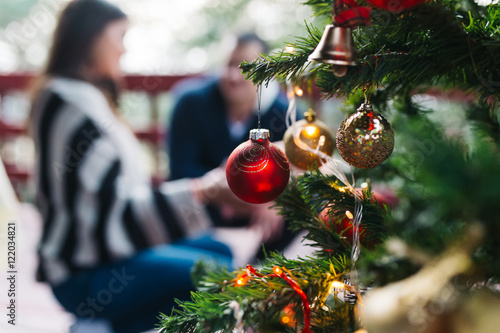 Christmas tree with ornamenst, with young couple in backgroung. photo