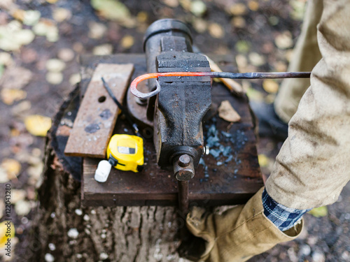 Blacksmith holds curved hot red iron rod in vise