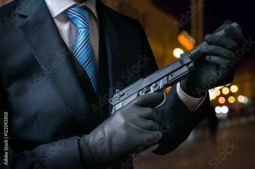 Hitman or assassin holds pistol with silencer in hands.