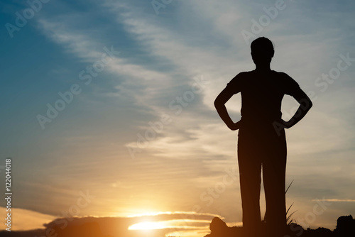 Silhouette of teenage girl standing at mountain in the sunset