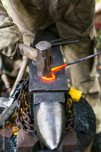 Blacksmith curves iron rod with hammer on anvi