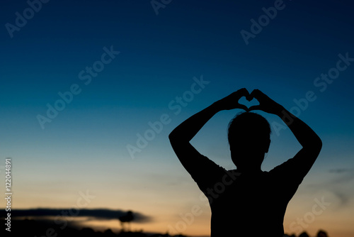 silhouette of woman Hand-made heart-shapedon on sky at sunset.