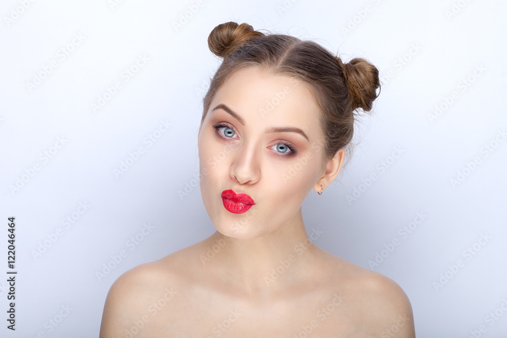 Portrait of a young pretty woman with trendy makeup bright red lips funny bun hairstyle and bare shoulders act the ape against white studio background Portrait of a young pretty woman with trendy makeup bright red lips funny bun hairstyle and bare shoulders act the ape against white studio background