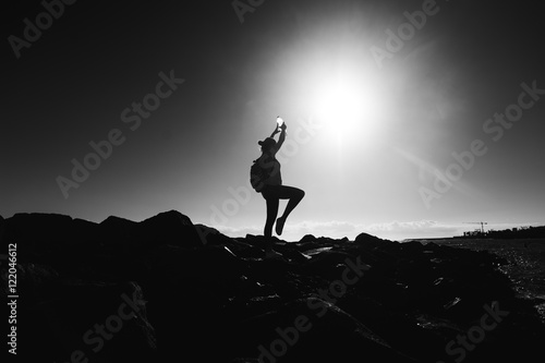 Silhouette of a young woman practicing yoga on a rocky shore