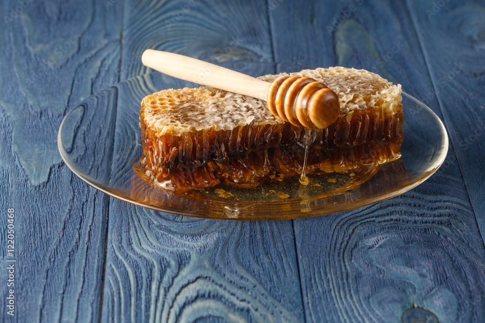 Honeycomb with honey dipper over dark blue surface Honeycomb with honey dipper over dark blue surface