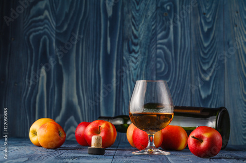 Glass with Calvados brandy and yellow apples on a wooden table photo