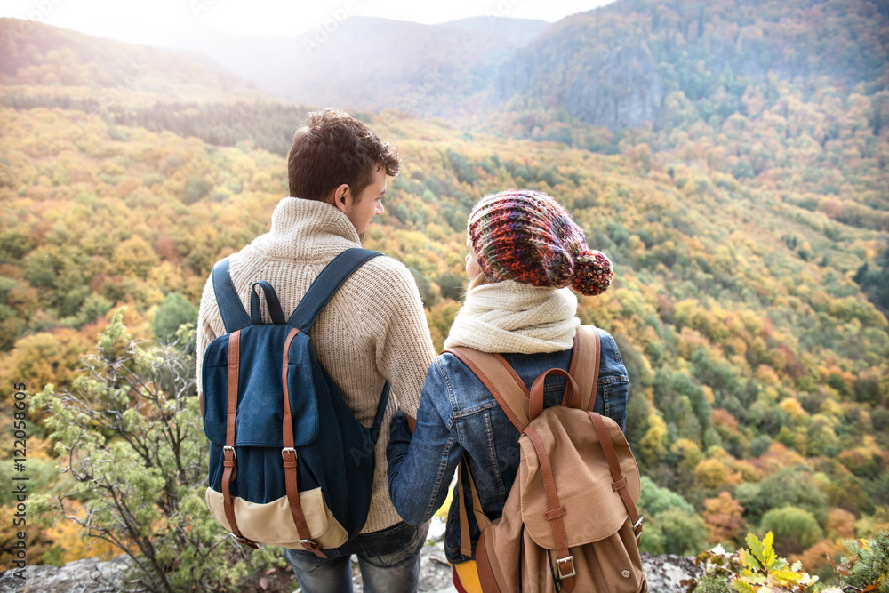 Beautiful couple with backpacks against colorful autumn forest