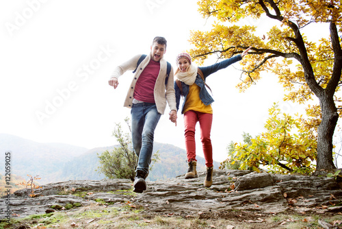 Beautiful couple in sunny autumn nature, running on a rock
