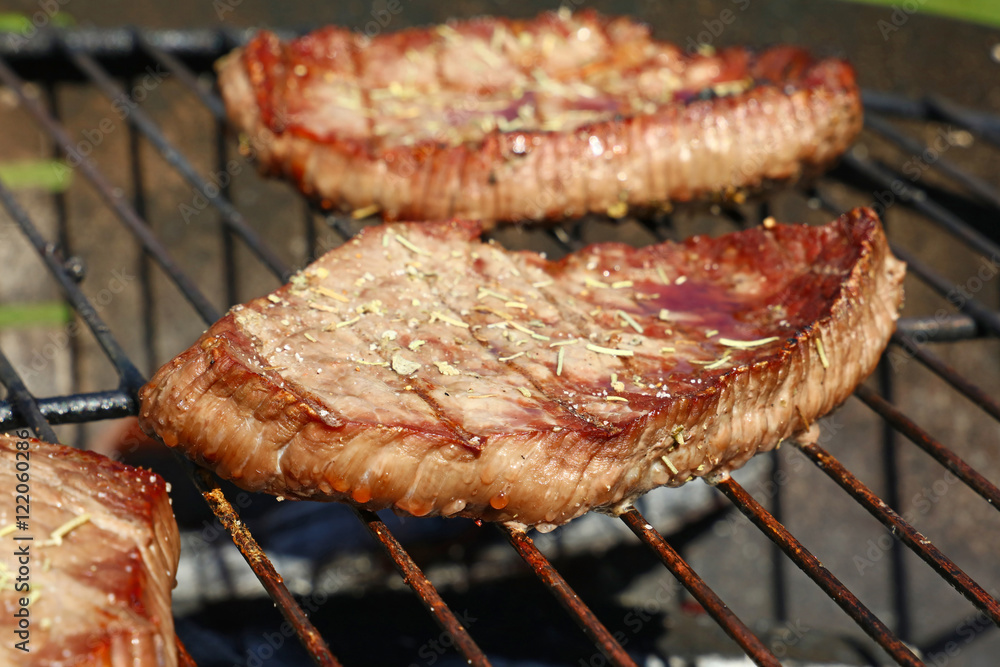 Grilled beef steaks cooking on barbecue grill