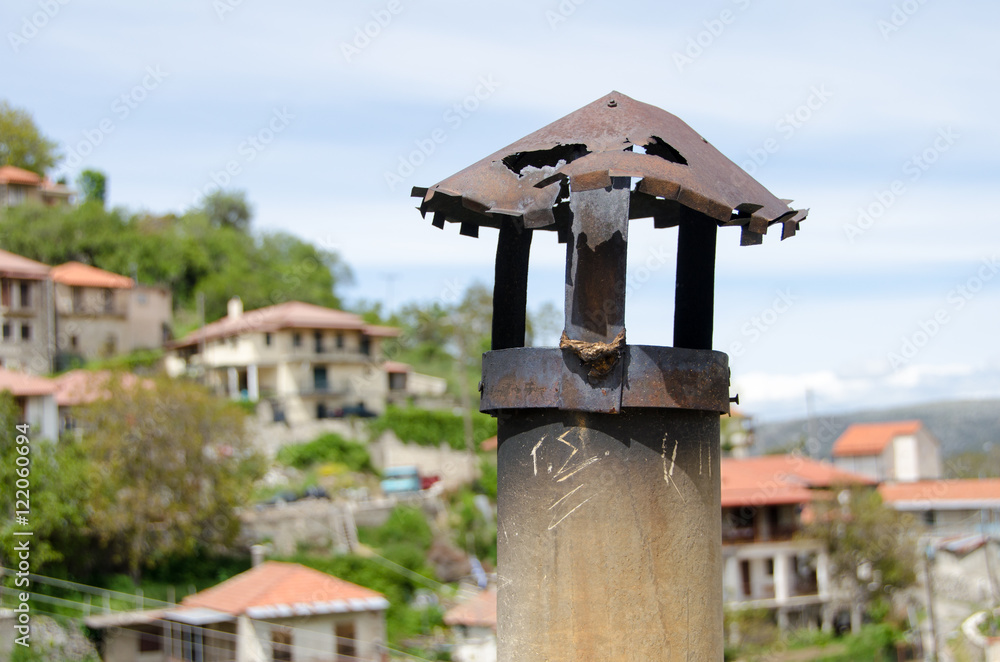Engraved letters on this old small rusty chimney with holes on the roof of a village house against sky. Baltessiniko village, Greece Engraved letters on this old small rusty chimney with holes on the roof of a village house against sky. Baltessiniko village, Greece