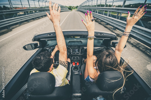 Couple of best friends with arms up at car trip on the road. photo