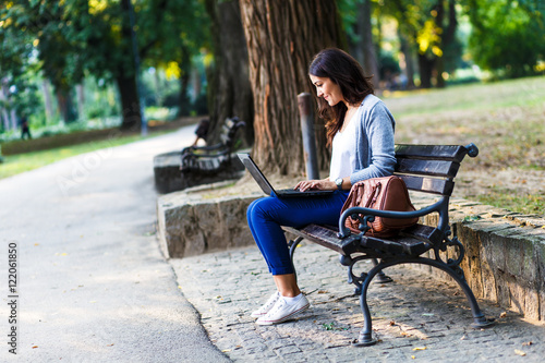 Young female student sitting on a bench in park, she is working on laptop. © Zoran Zeremski