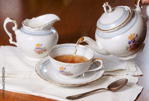 Tea being poured into cup, set on wood