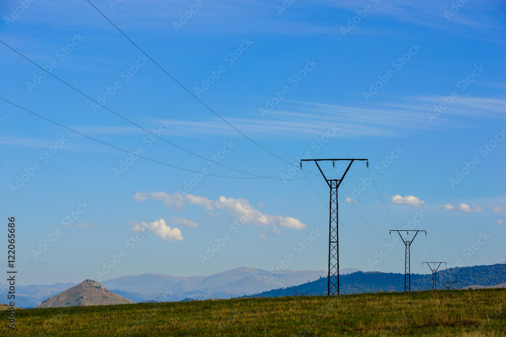 Beautiful photograph of a row of transmission towers and power lines against a blue cloudy sky, Armenia