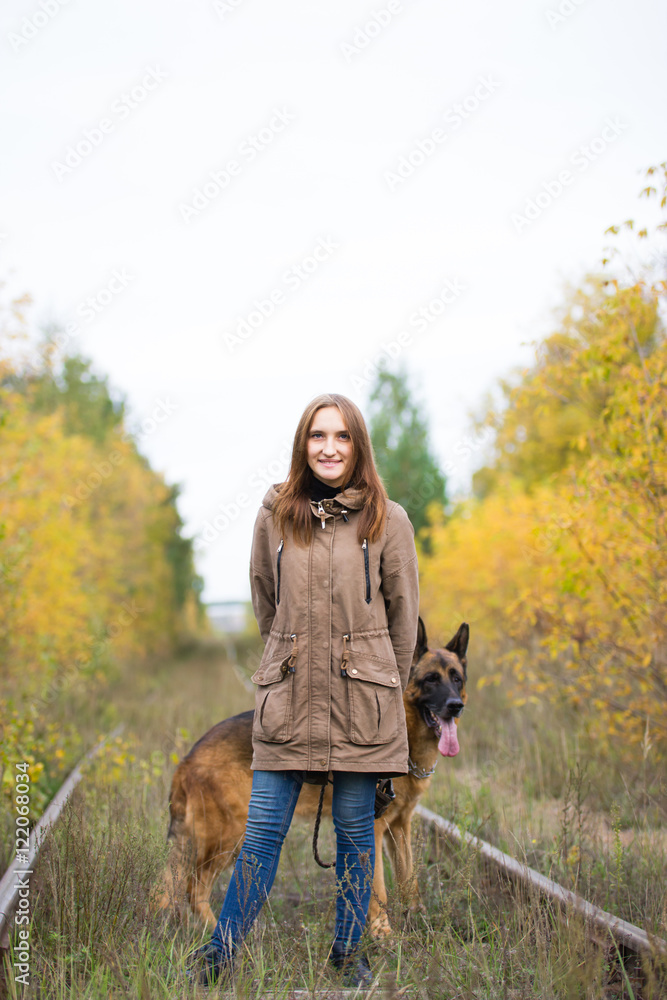 Young cute woman with german shepherd dog posing in autumn forest near rail way