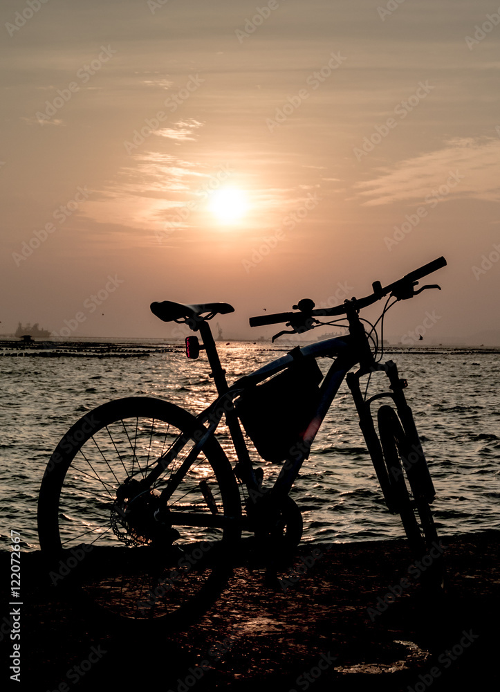 Silhouette of mountain bike at sea with sunset sky background