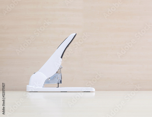 Closeup white stapler , office equipment on blurred wood desk and wall in office room textured background under window light