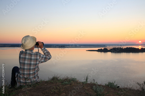 мальчик смотрит в бинокль на восход солнца на реке