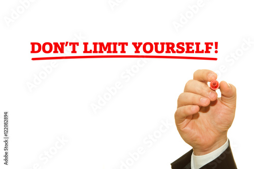 Businessman hand writing DON'T LIMIT YOURSELF message on a transparent wipe board.