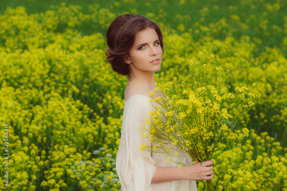 Portrait of young beautiful girl in field with bouquet of yellow flowers in hands looking to the camera Portrait of young beautiful girl in field with bouquet of yellow flowers in hands looking to the camera