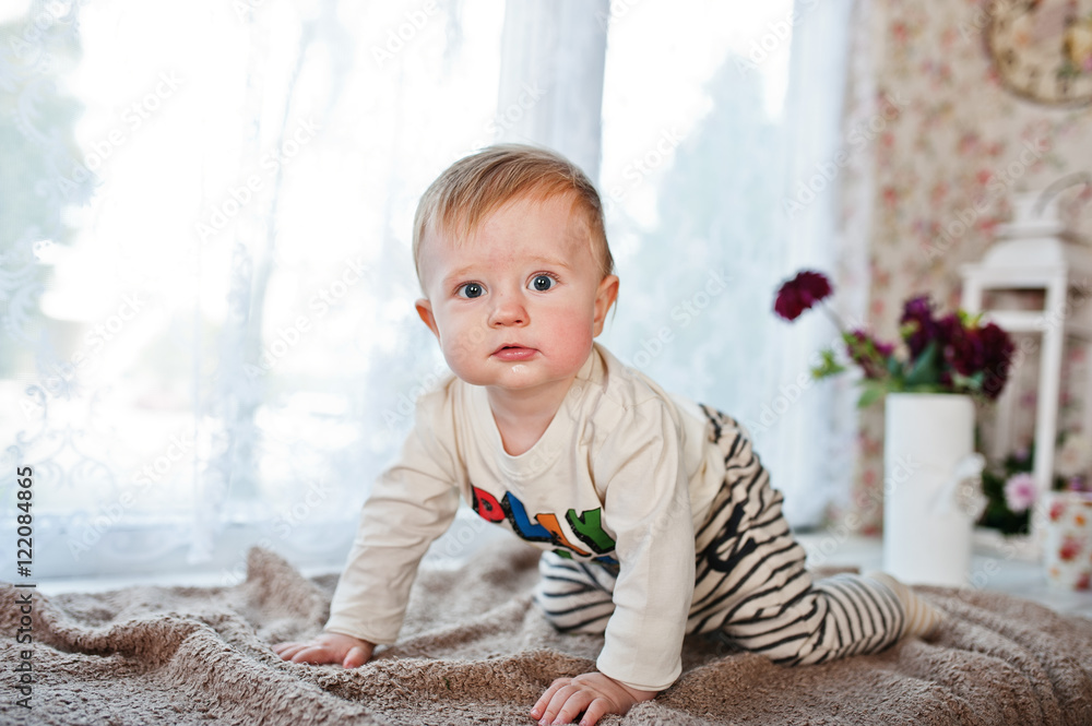 Fototapeta premium Cute little caucasian baby boy creeps on coverlet and looking at