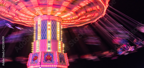 people  spinning around fast and high in swings at the brightly lit ride at the county fair 
