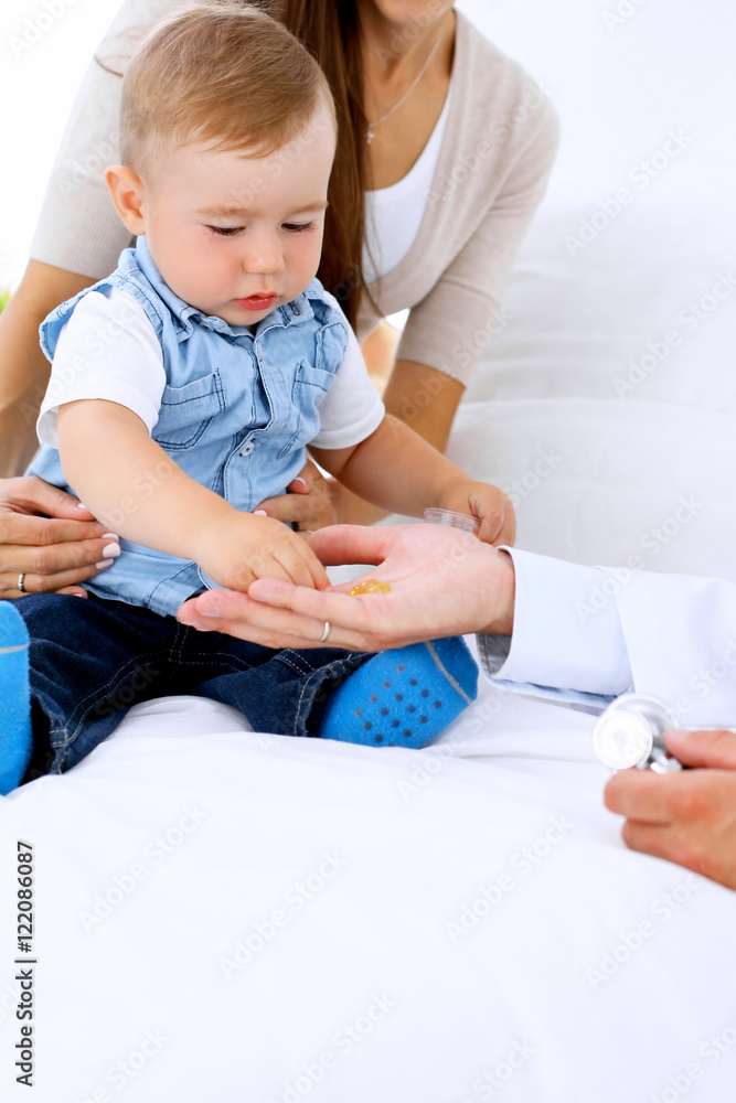 Little boy child  with his mother  at  health exam at doctor's office. Patient takes pills from physician's hand
