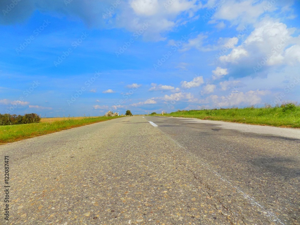 Asphalt road between fields during sunny day