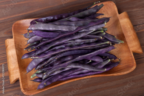 purple string beans on a wooden plate on a wooden background