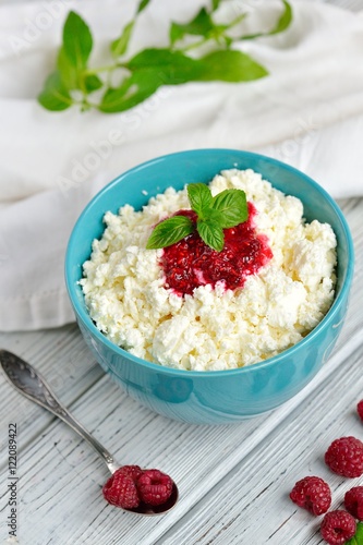 Cottage cheese in blue bowl with raspberries jam and mint on wooden background