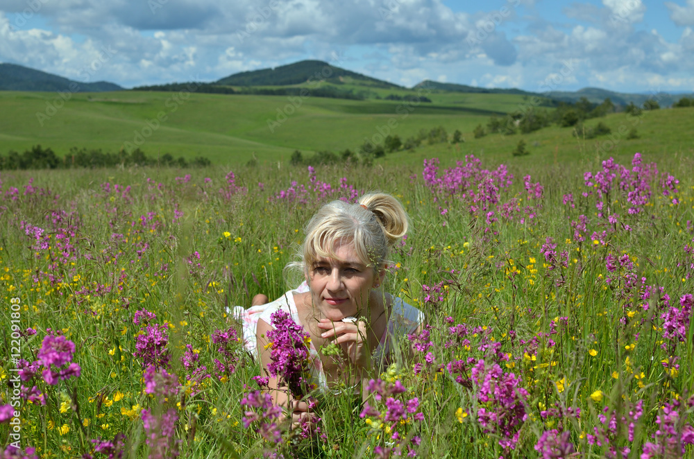 Lady lying in a meadow, surrounded by wildflowers and holding a bouquet of pink flowers Lady lying in a meadow, surrounded by wildflowers and holding a bouquet of pink flowers