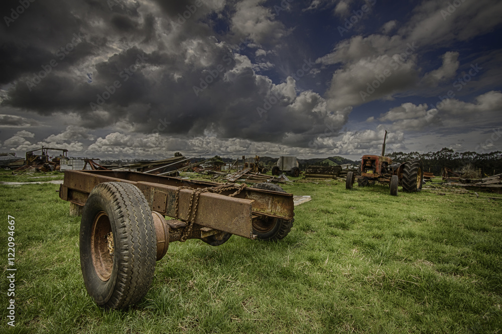Fototapeta premium Old agricultural machinery in a field under a dynamic cloudy blue sky 