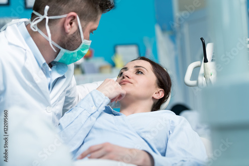 Dentist examining Patient teeth with a Mouth Mirror. Dentist is a Man, Patient is a Woman. Patient is Relaxed and not scared of Dentist.