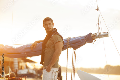 Handsome man on sailing boat in sunset.