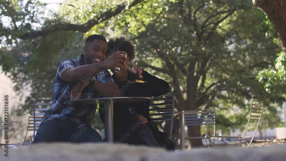 African American couple sitting at an outdoor table and taking pictures with a cell phone, bokeh African American couple sitting at an outdoor table and taking pictures with a cell phone, bokeh
