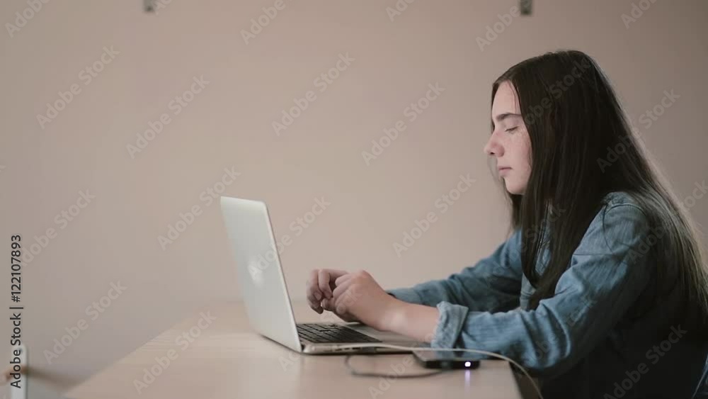 Portrait of a girl teenager student using a laptop surfing the Internet while sitting at the table at home Portrait of a girl teenager student using a laptop surfing the Internet while sitting at the table at home