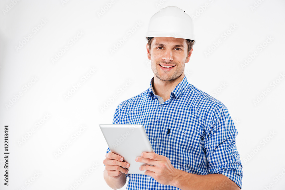Cheerful man architect in hard hat standing and using tablet Cheerful man architect in hard hat standing and using tablet
