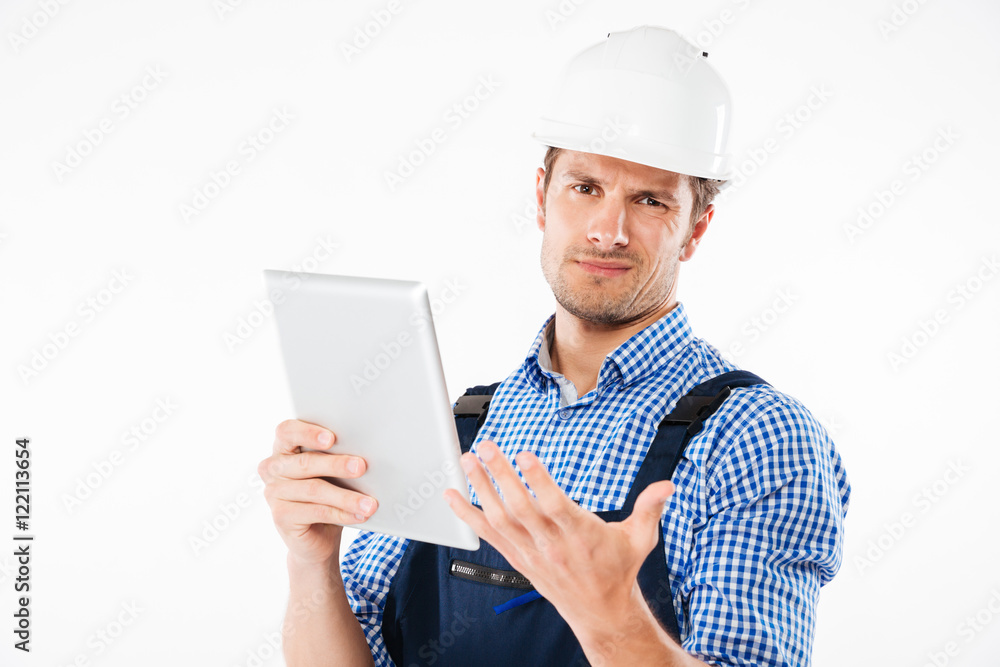 Confused builder in helmet scratching his head and holding tablet Confused builder in helmet scratching his head and holding tablet