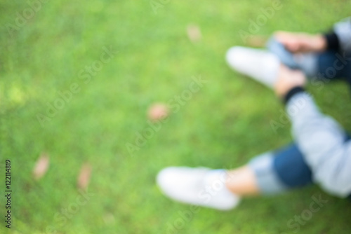 hands with long sleeve shirt holding mobile phone, sitting on green grass lawn, blurred