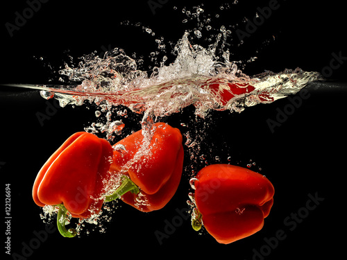 Group of bell pepper falling in water with splash on black backg