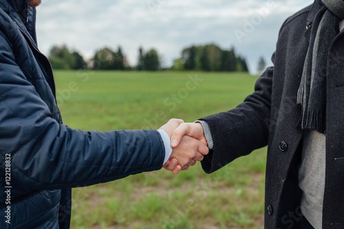 A men's hand giving a handshake. Outdoor background.