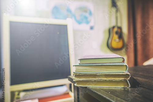 Books lying on a table in a classroom at a private school with a black board, card and guitar on the wall