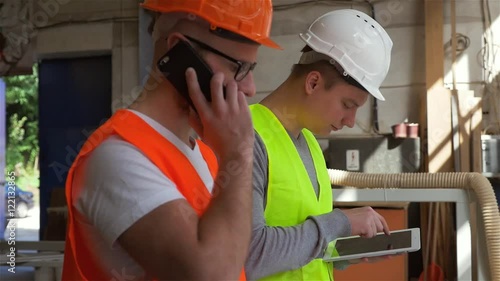 Two carpenters are analyzing conctruction plans by using tablet pc. One of them is talking by the phone. photo